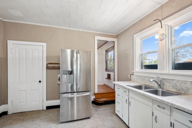kitchen with stainless steel refrigerator with ice dispenser, a sink, crown molding, white cabinets, and light countertops