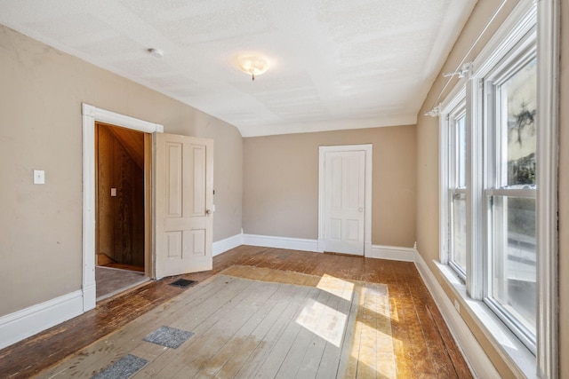 empty room with wood-type flooring, plenty of natural light, baseboards, a smoke detector, and a textured ceiling