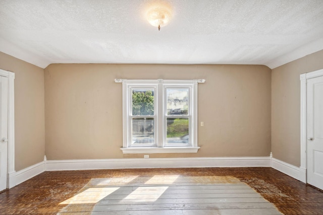 empty room featuring a textured ceiling, baseboards, vaulted ceiling, and wood-type flooring