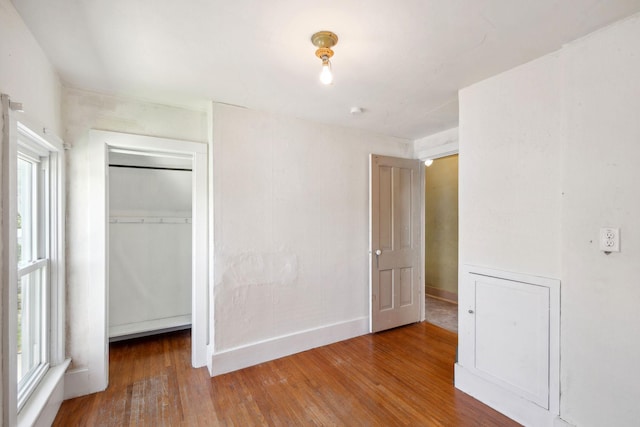 unfurnished bedroom featuring wood finished floors, multiple windows, a closet, and baseboards