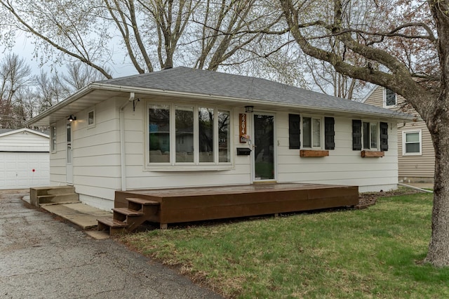 view of front of home featuring an outbuilding, roof with shingles, a garage, and a front yard