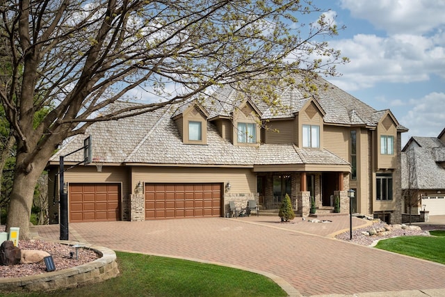 view of front facade featuring decorative driveway, a porch, an attached garage, and stone siding