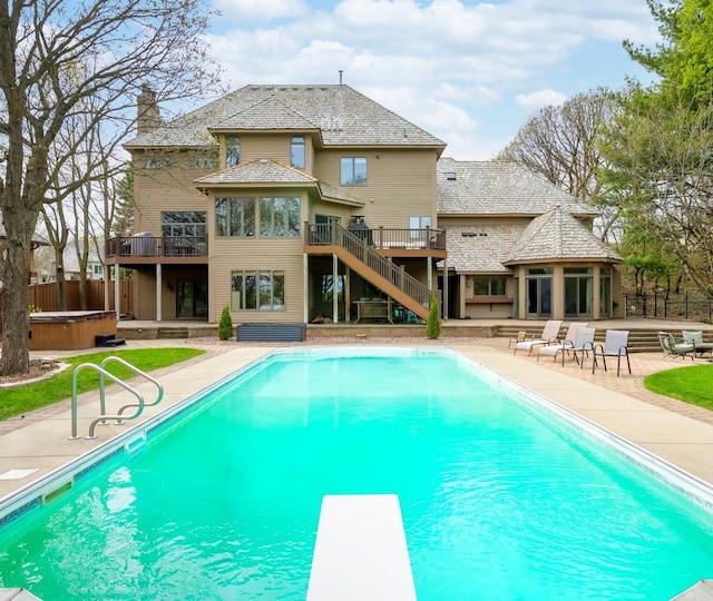 swimming pool featuring a hot tub, a patio area, a wooden deck, a diving board, and stairs