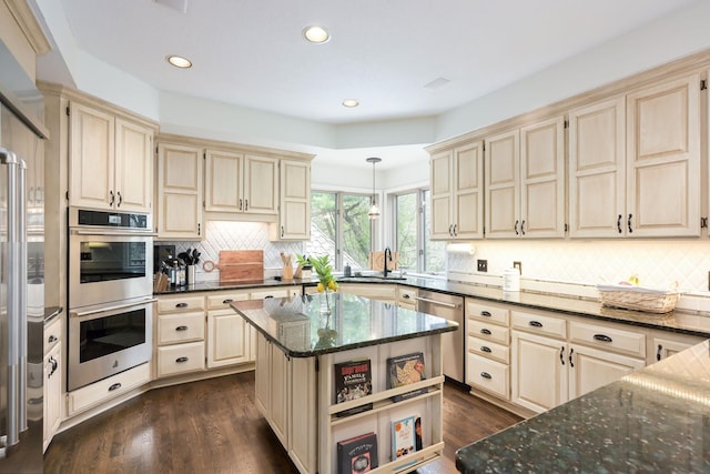 kitchen featuring appliances with stainless steel finishes, cream cabinetry, dark stone countertops, tasteful backsplash, and recessed lighting