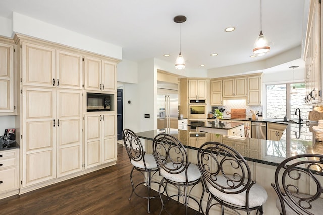kitchen with built in appliances, a breakfast bar area, a sink, decorative backsplash, and dark wood-style floors