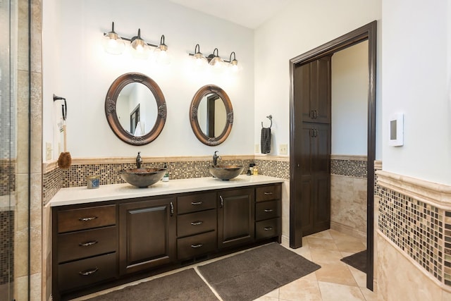 bathroom with tile walls, double vanity, a wainscoted wall, and tile patterned floors