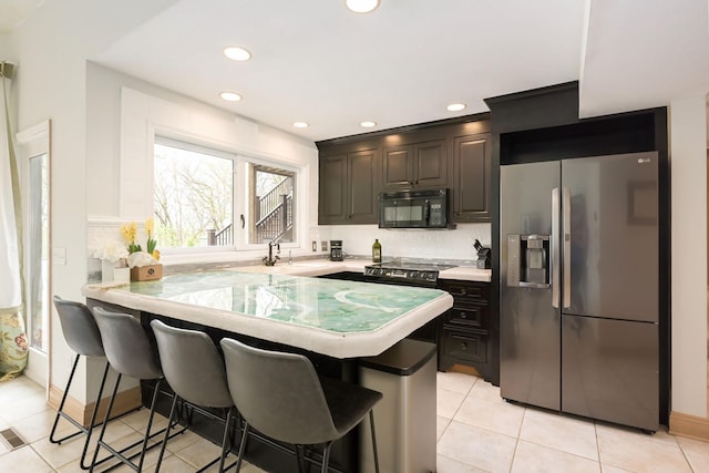 kitchen with stainless steel fridge, black microwave, a breakfast bar, a sink, and light countertops