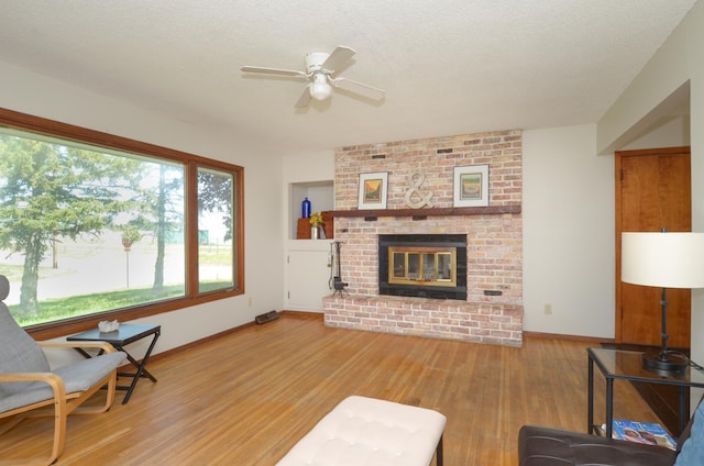 living area featuring a ceiling fan, light wood finished floors, a fireplace, baseboards, and a textured ceiling