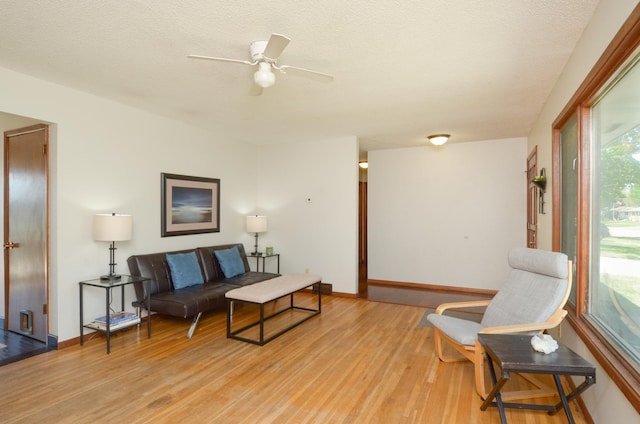 living room with light wood-style floors, ceiling fan, baseboards, and a textured ceiling