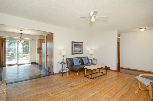 living area featuring ceiling fan, light wood finished floors, baseboards, and a textured ceiling