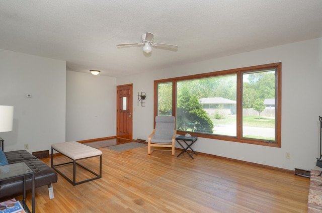 living area featuring ceiling fan, light wood-style flooring, and baseboards