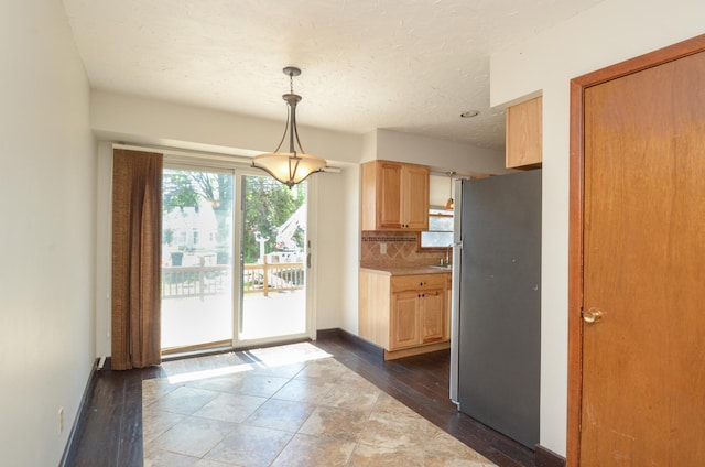 kitchen featuring freestanding refrigerator, light brown cabinetry, backsplash, light countertops, and pendant lighting