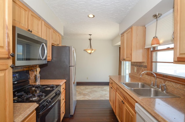 kitchen with black gas stove, stainless steel microwave, a sink, baseboards, and light brown cabinetry