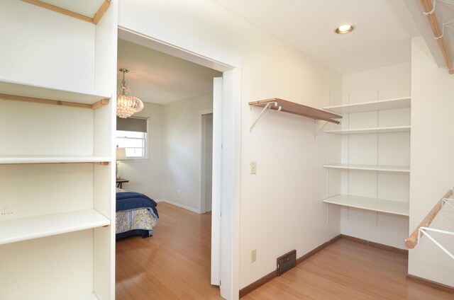 walk in closet with light wood-type flooring and a chandelier