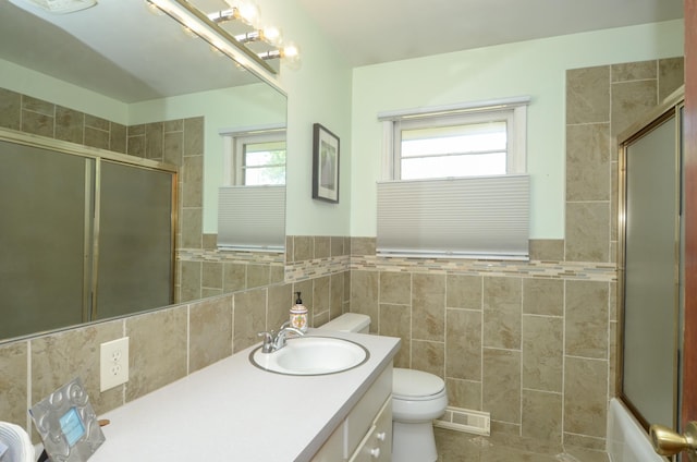 full bathroom featuring a shower with shower door, tile walls, toilet, vanity, and a wainscoted wall