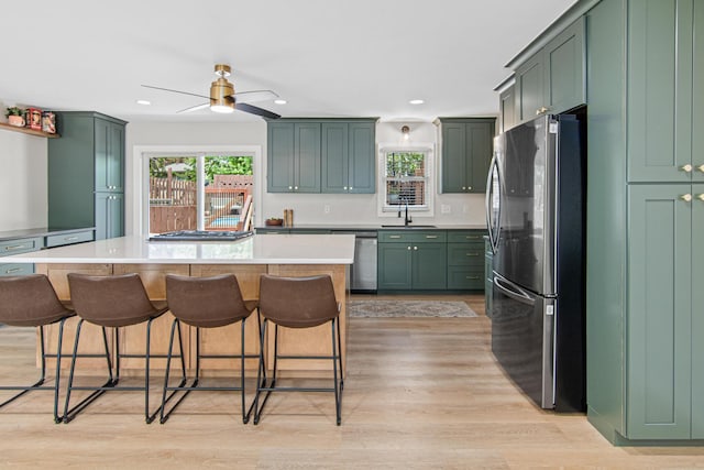 kitchen with appliances with stainless steel finishes, a sink, light wood finished floors, a kitchen bar, and recessed lighting