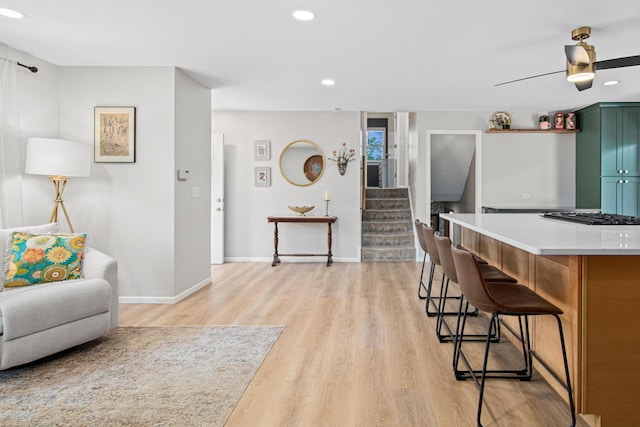 kitchen featuring green cabinets, light wood finished floors, a breakfast bar area, baseboards, and recessed lighting