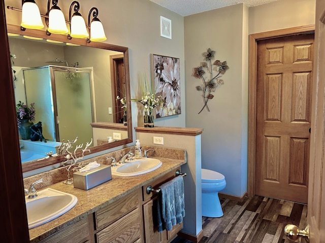 bathroom with wood finished floors, a shower stall, toilet, double vanity, and a textured ceiling