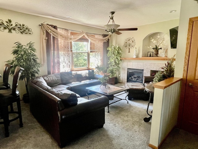 living area featuring carpet flooring, a textured ceiling, ceiling fan, and a tile fireplace