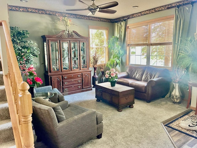 living room with carpet flooring, a ceiling fan, and stairs