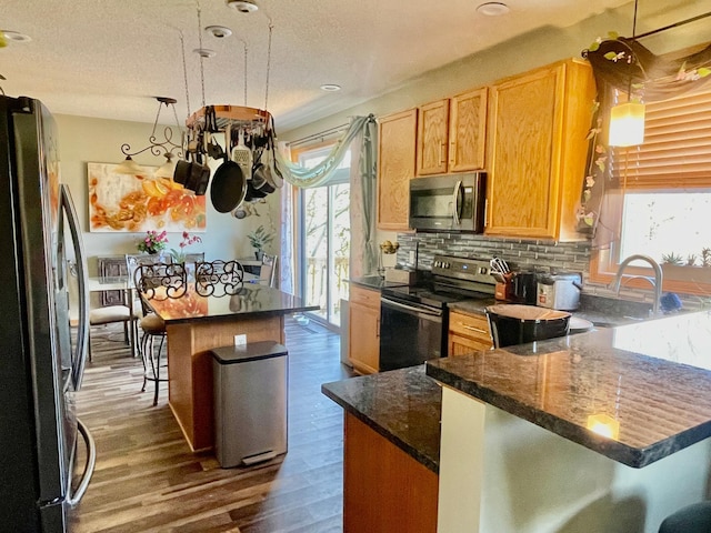 kitchen with dark wood finished floors, a kitchen bar, a peninsula, backsplash, and appliances with stainless steel finishes