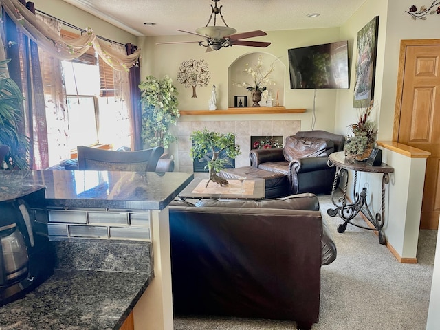 carpeted living area featuring a tile fireplace, ceiling fan, and a textured ceiling