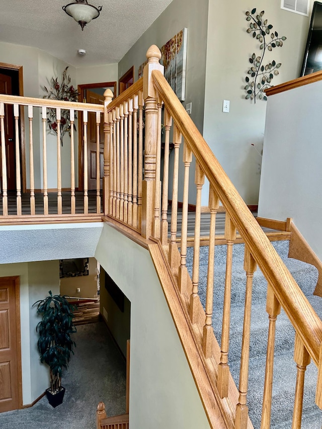 staircase featuring a water view, carpet flooring, visible vents, and a textured ceiling