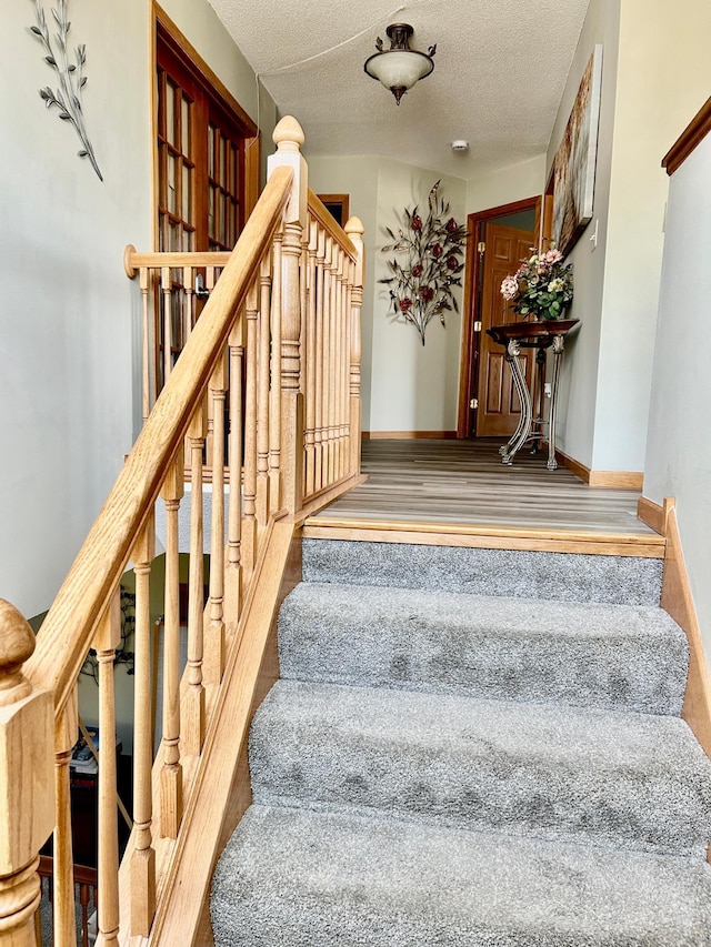 stairway featuring carpet, a textured ceiling, and baseboards