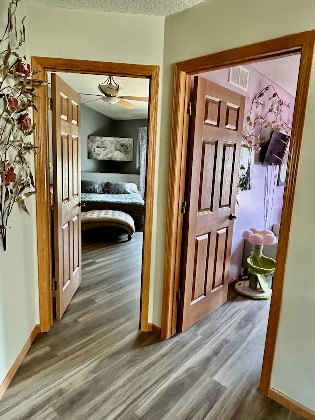 hallway with baseboards, visible vents, a textured ceiling, and wood finished floors