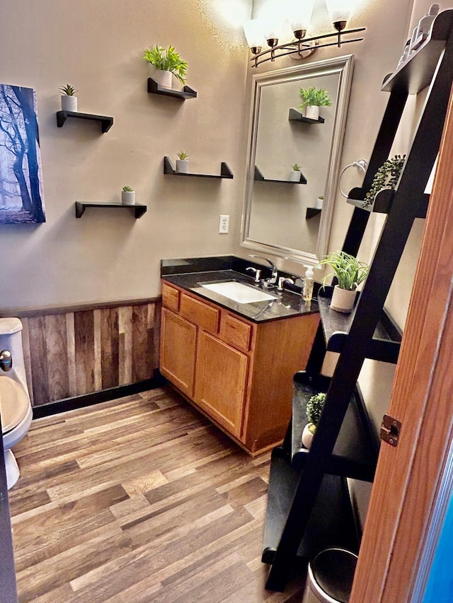 half bathroom featuring a wainscoted wall, toilet, wood finished floors, and vanity