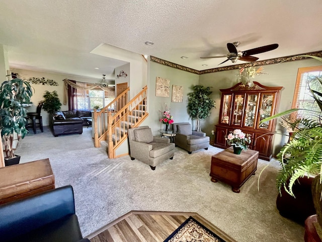 living room featuring wood finished floors, carpet floors, a textured ceiling, ceiling fan, and stairs