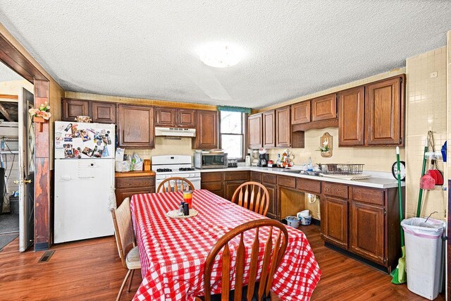 kitchen with white appliances, under cabinet range hood, dark wood-style floors, light countertops, and a textured ceiling