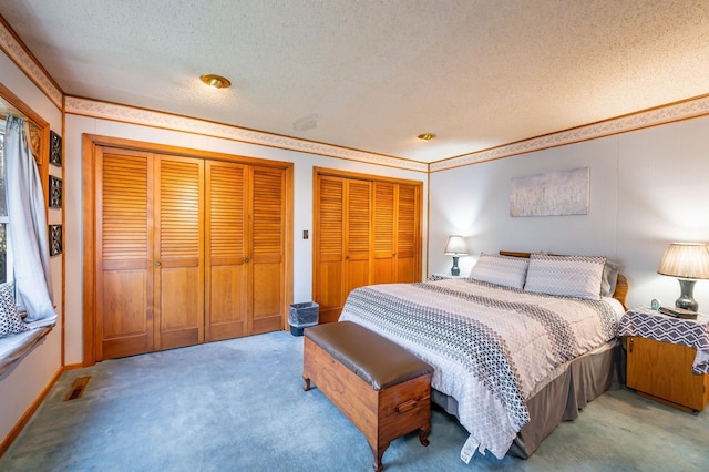 bedroom with two closets, a textured ceiling, carpet flooring, and ornamental molding