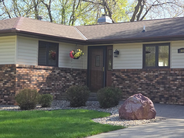 view of exterior entry with a shingled roof and a chimney