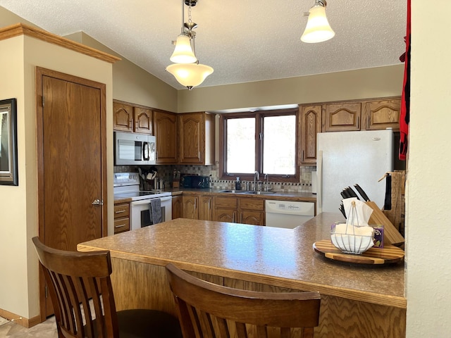 kitchen featuring a breakfast bar, white appliances, a sink, a peninsula, and tasteful backsplash