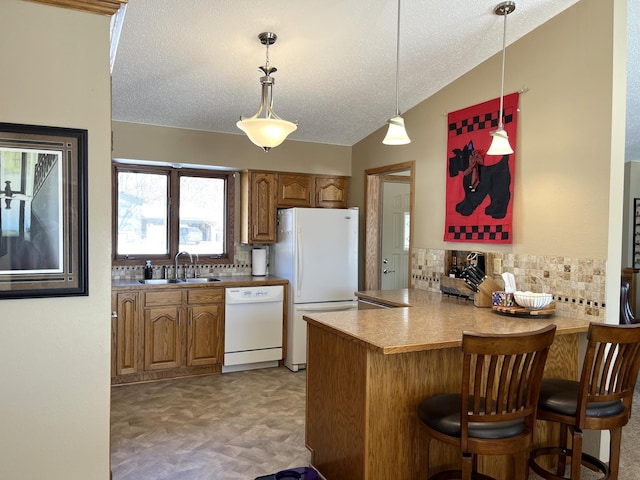kitchen with a peninsula, a sink, brown cabinetry, white appliances, and decorative backsplash
