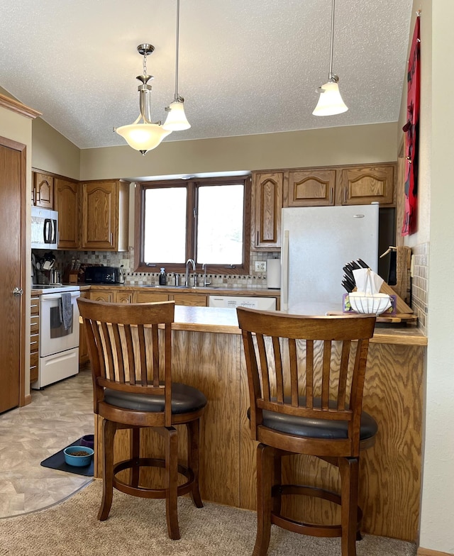 kitchen featuring a kitchen breakfast bar, a textured ceiling, white appliances, and decorative backsplash