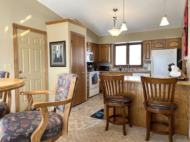 kitchen featuring hanging light fixtures, a kitchen breakfast bar, a textured ceiling, white appliances, and light carpet