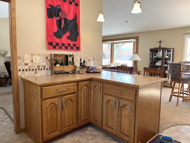 kitchen with brown cabinetry, backsplash, light carpet, and a textured ceiling