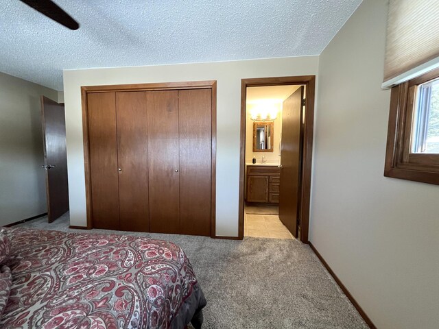 bedroom with ensuite bathroom, light carpet, a textured ceiling, and a closet