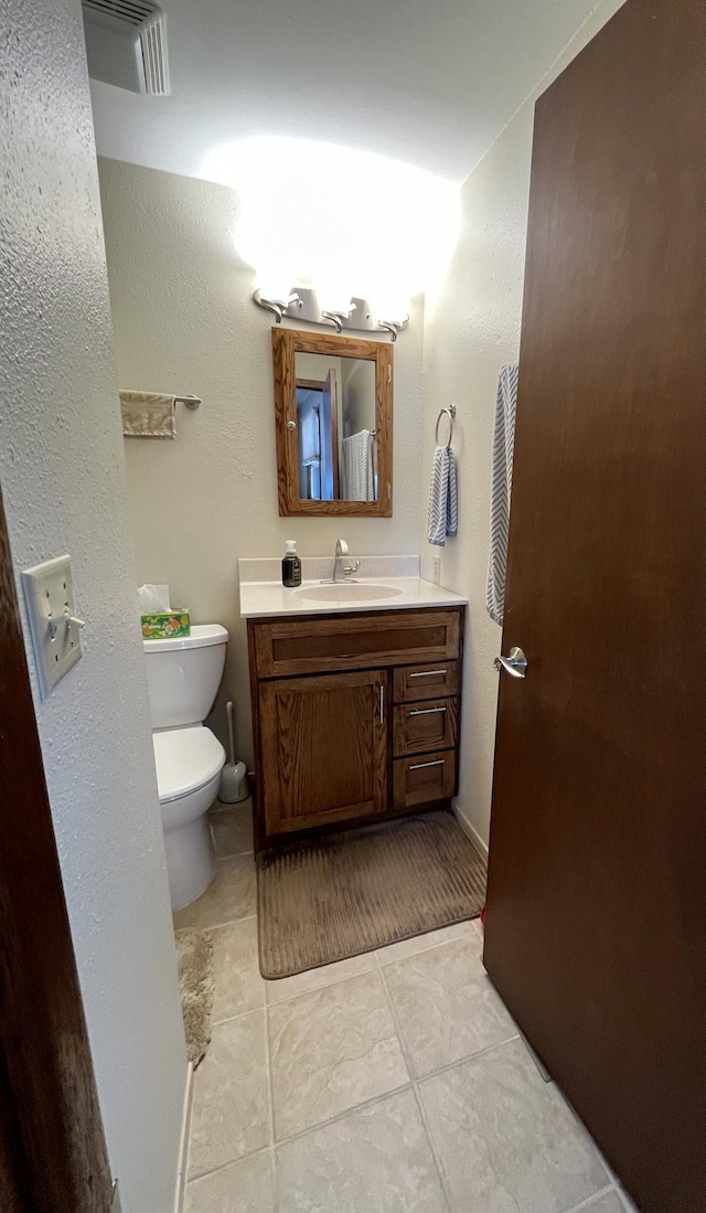 half bath with toilet, visible vents, tile patterned flooring, and vanity