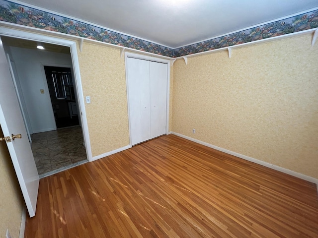 324 Maple Ave S, Thief River Falls, MN 56701 - unfurnished bedroom featuring wood finished floors, a closet, wallpapered walls, and baseboards