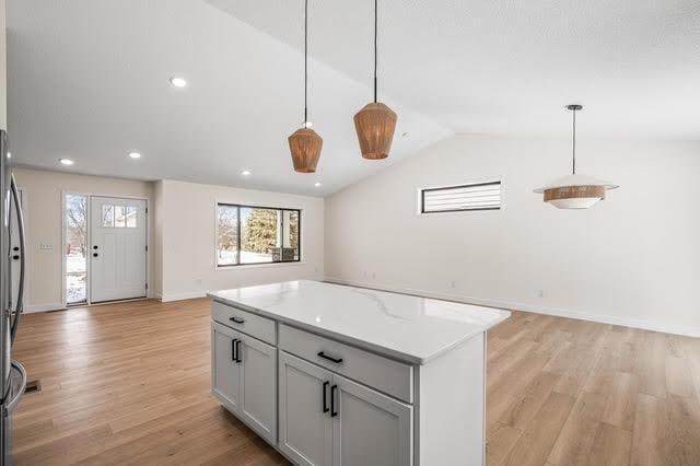 2140 Arkwright St, Maplewood, MN 55117 - kitchen featuring open floor plan, light wood-type flooring, vaulted ceiling, decorative light fixtures, and a kitchen island