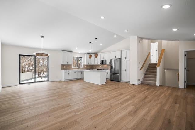 kitchen featuring stainless steel appliances, open floor plan, white cabinets, a kitchen island, and backsplash