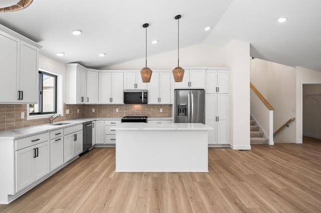 kitchen with appliances with stainless steel finishes, vaulted ceiling, white cabinetry, light countertops, and backsplash