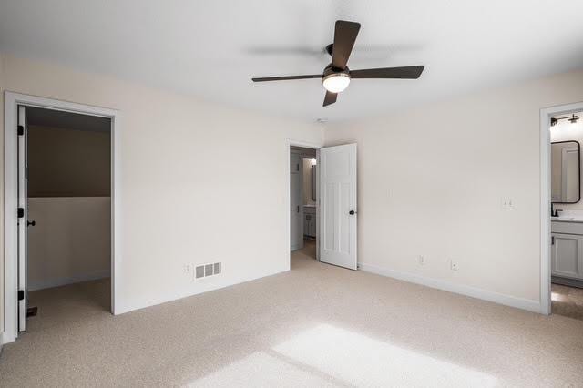 unfurnished bedroom with light carpet, a spacious closet, ensuite bath, a closet, and ceiling fan