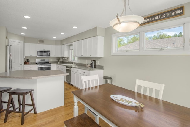 5057 Linden Trl N, Lake Elmo, MN 55042 - kitchen with stainless steel appliances, a sink, a kitchen bar, light wood-style flooring, and white cabinets
