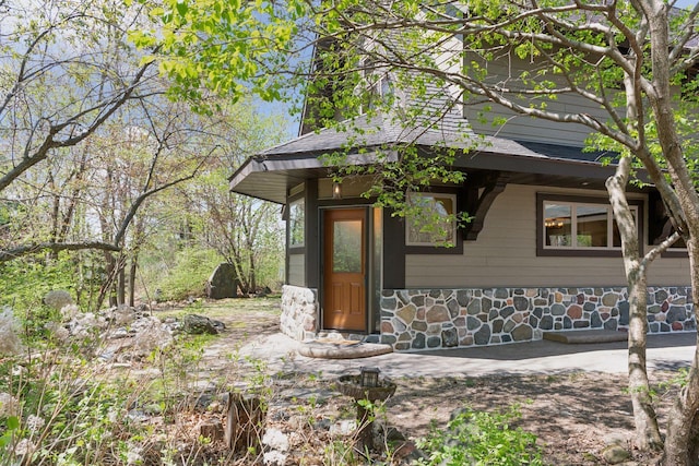 entrance to property featuring stone siding and roof with shingles