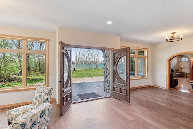 foyer entrance featuring arched walkways, baseboards, a chandelier, light wood finished floors, and a textured ceiling