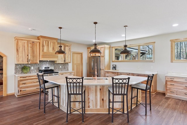 kitchen featuring stainless steel appliances, light brown cabinetry, an island with sink, tasteful backsplash, and light countertops